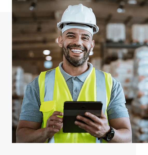 Smiling construction worker wearing a helmet and safety vest using a tablet.